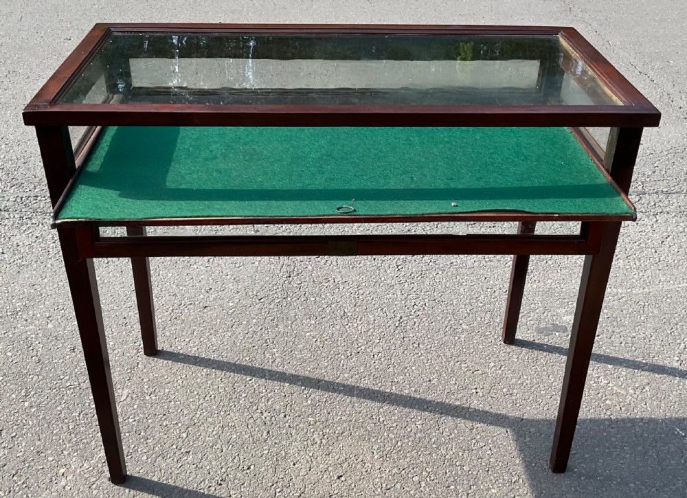 An Edwardian mahogany display table featuring a rectangular glass top, glazed sides, a green baize interior base, and slender square tapered legs. View VI