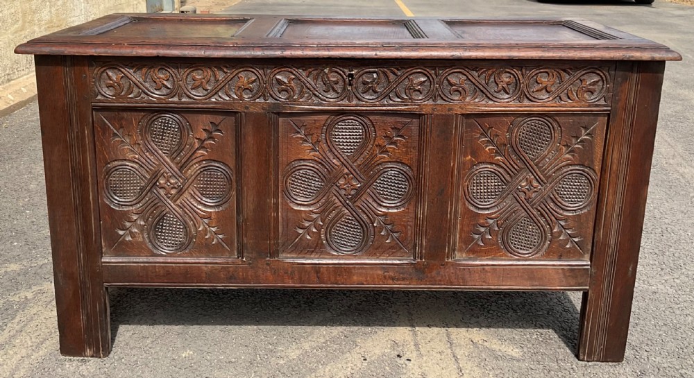 An antique dark oak blanket chest featuring three relief-carved front panels, a carved upper frieze, and a three-panel hinged top.