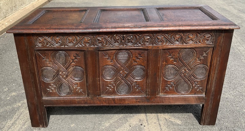 An antique dark oak blanket chest featuring three relief-carved front panels, a carved upper frieze, and a three-panel hinged top. View VI