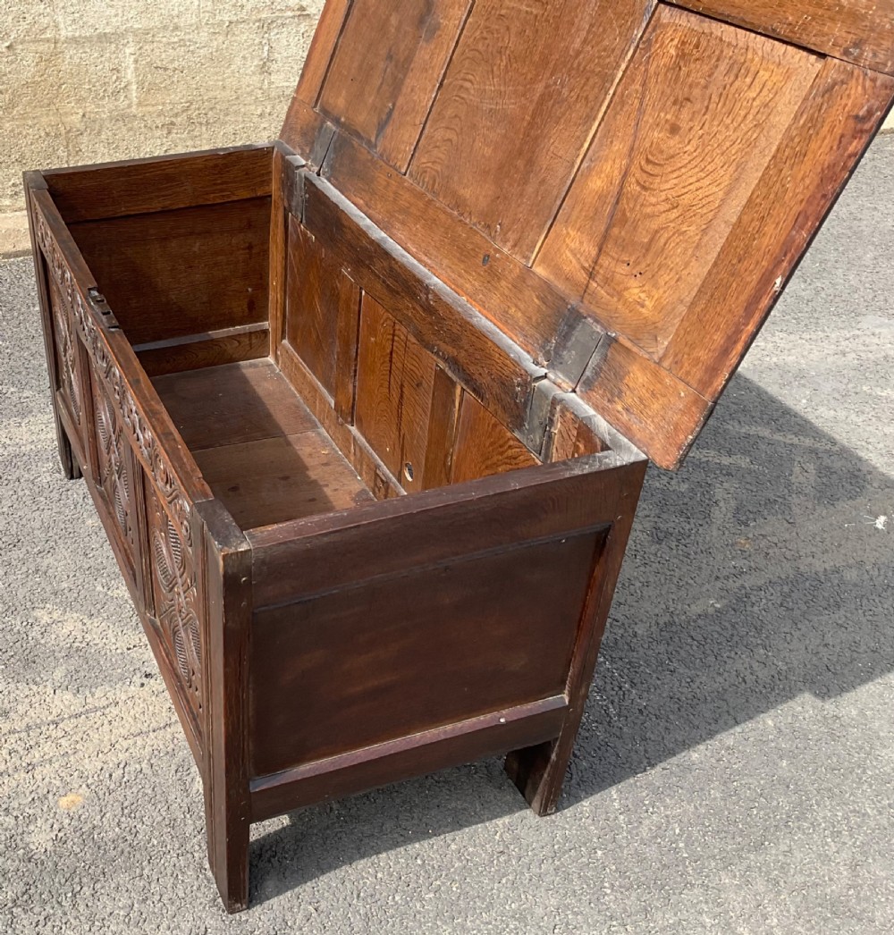 An antique dark oak blanket chest featuring three relief-carved front panels, a carved upper frieze, and a three-panel hinged top. View VIII