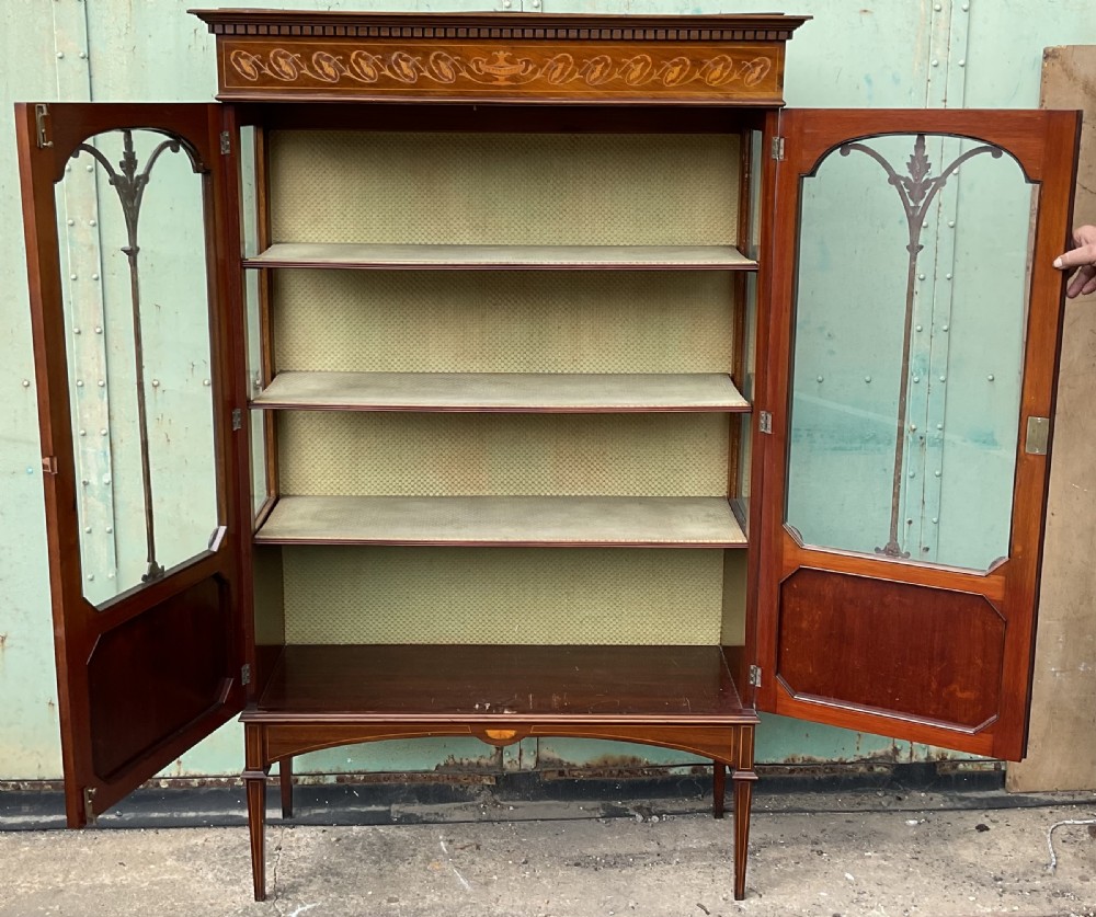 An Edwardian inlaid mahogany display cabinet featuring two glazed doors with decorative glazing bars, an inlaid urn frieze, and square tapered legs. View VII