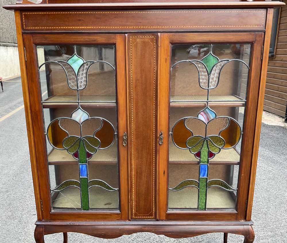 An Edwardian mahogany display cabinet featuring leaded stained glass doors with floral motifs, satinwood inlay, and cabriole legs. View V