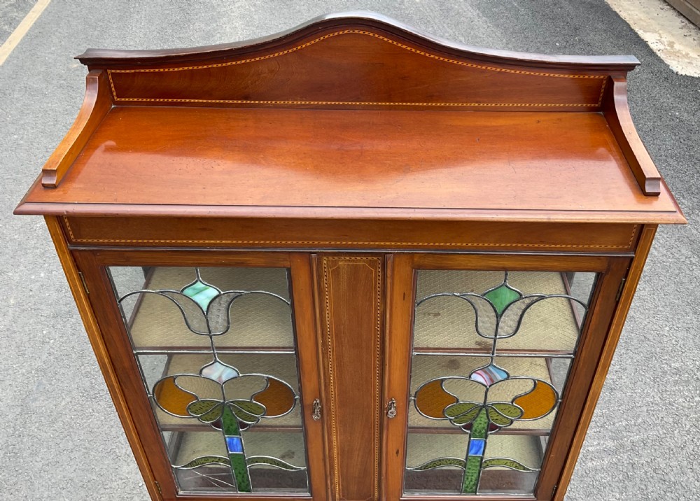 An Edwardian mahogany display cabinet featuring leaded stained glass doors with floral motifs, satinwood inlay, and cabriole legs. View VI