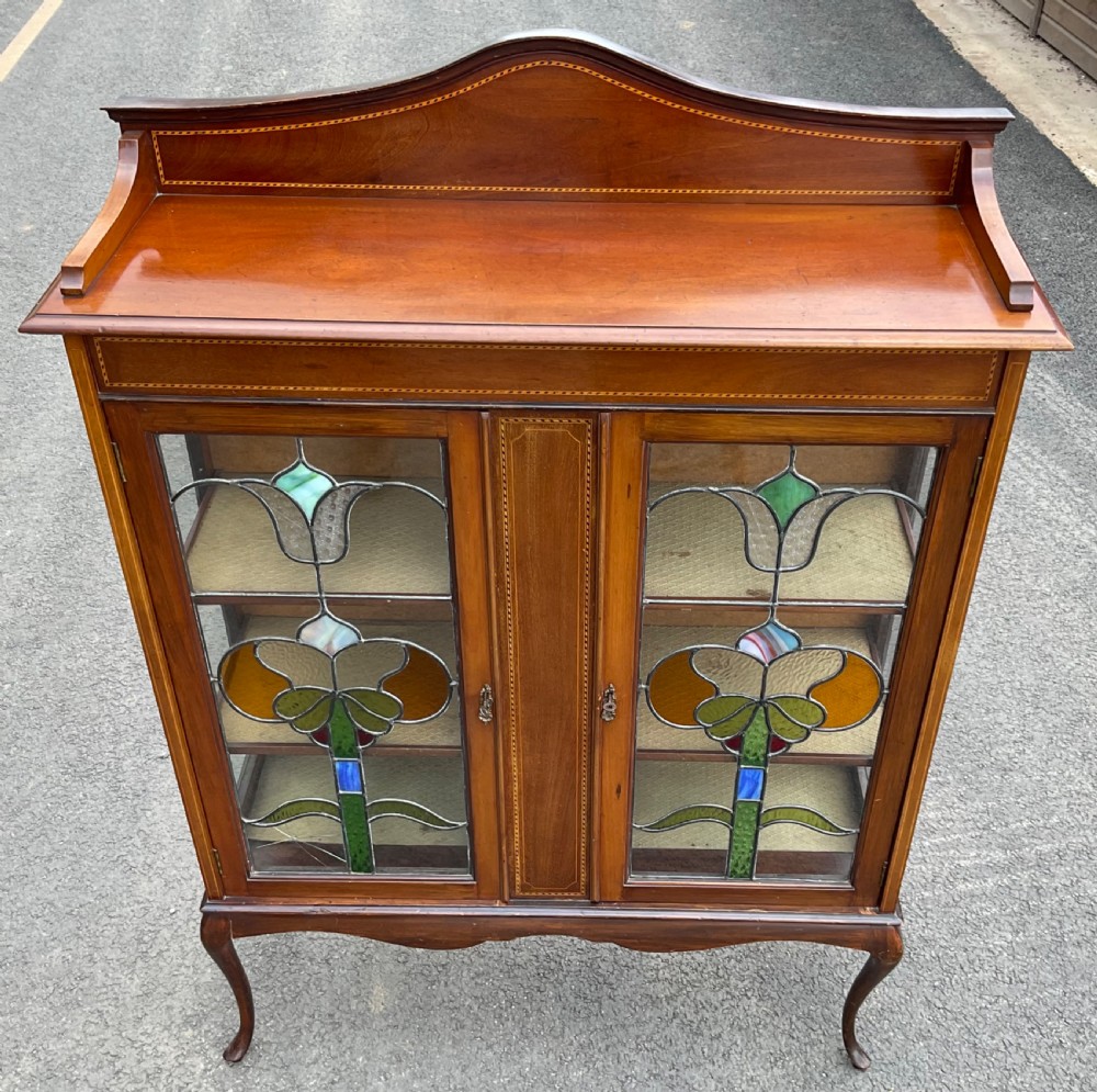 An Edwardian mahogany display cabinet featuring leaded stained glass doors with floral motifs, satinwood inlay, and cabriole legs. View VII