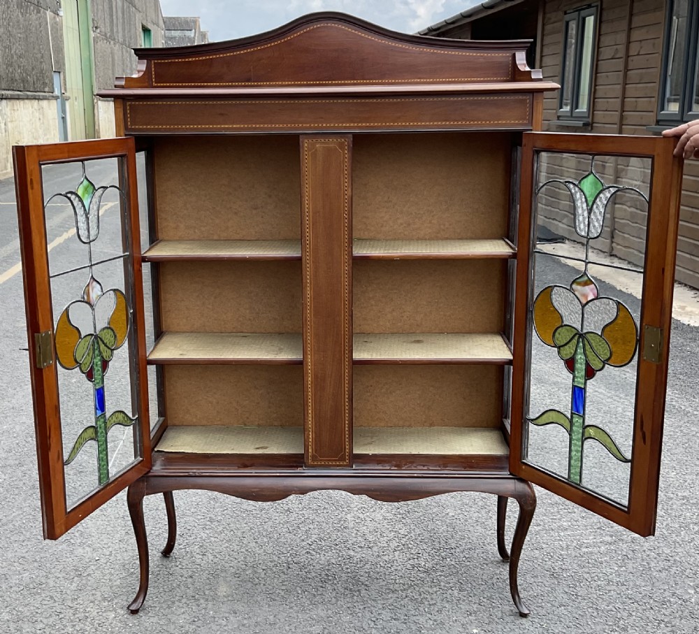 An Edwardian mahogany display cabinet featuring leaded stained glass doors with floral motifs, satinwood inlay, and cabriole legs. View VIII