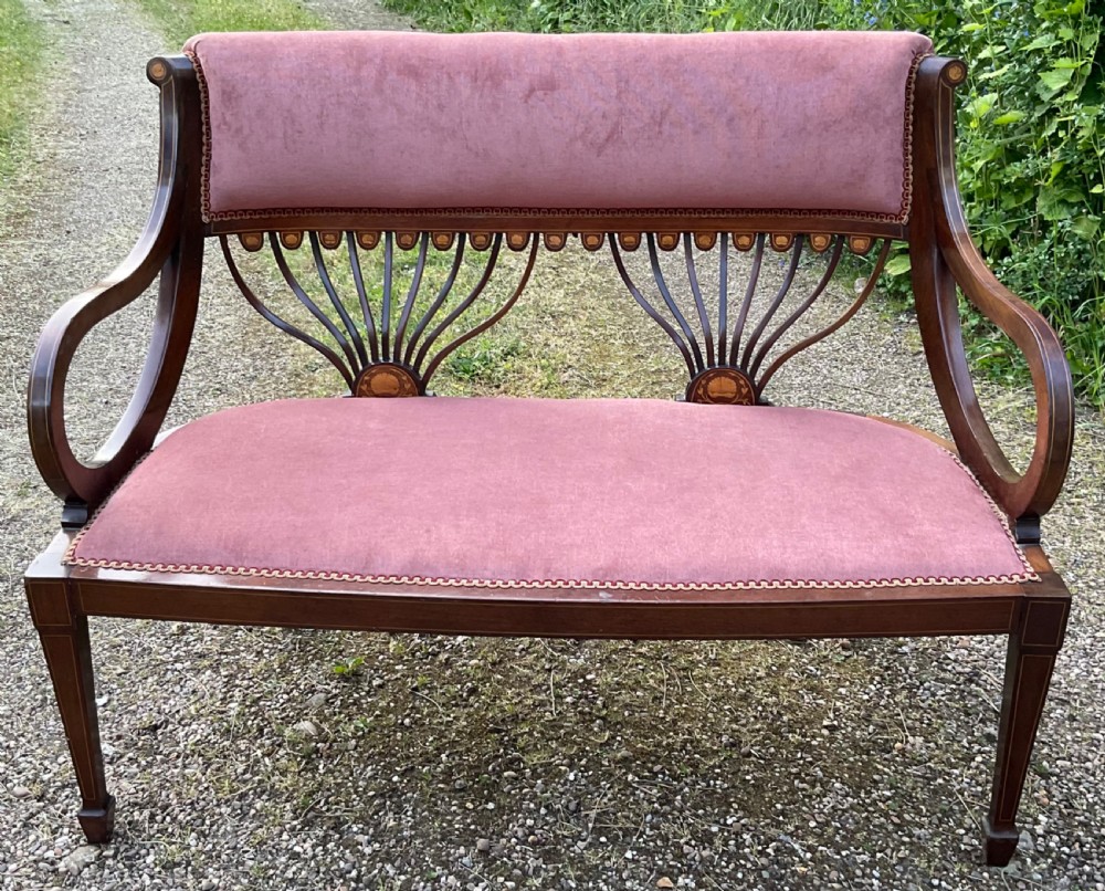 An Edwardian inlaid mahogany salon settee featuring a padded dusty pink velvet backrest and seat, flanked by sweeping arms and supported by splats with fan-shaped inlay. View II