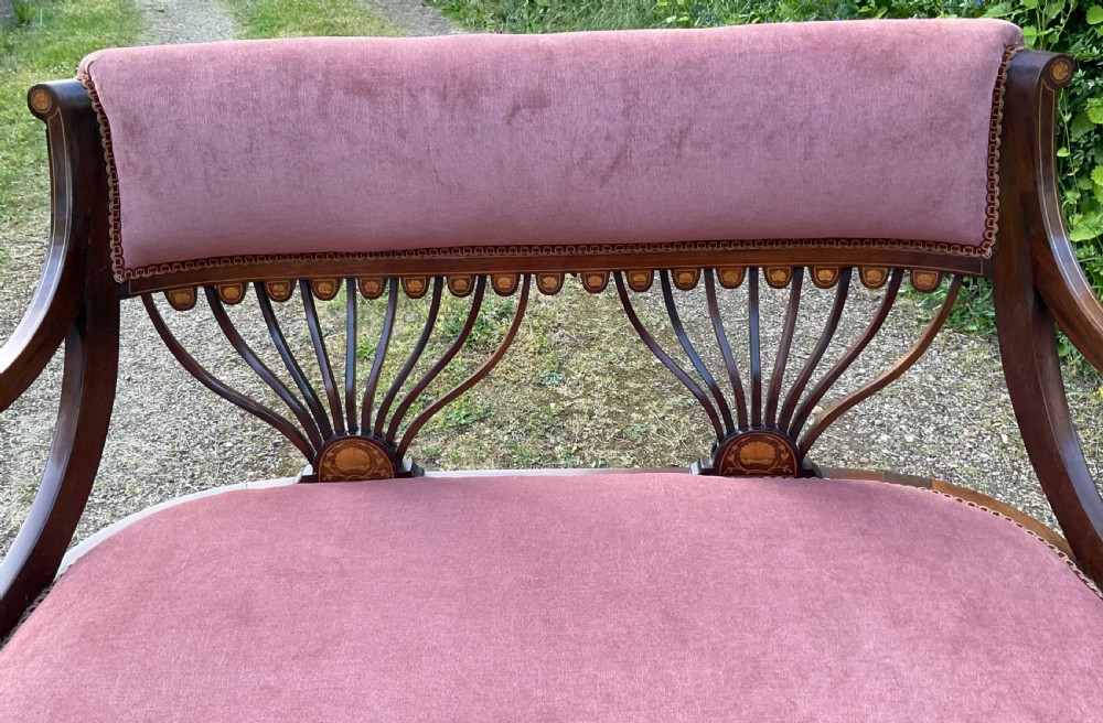 An Edwardian inlaid mahogany salon settee featuring a padded dusty pink velvet backrest and seat, flanked by sweeping arms and supported by splats with fan-shaped inlay. View III