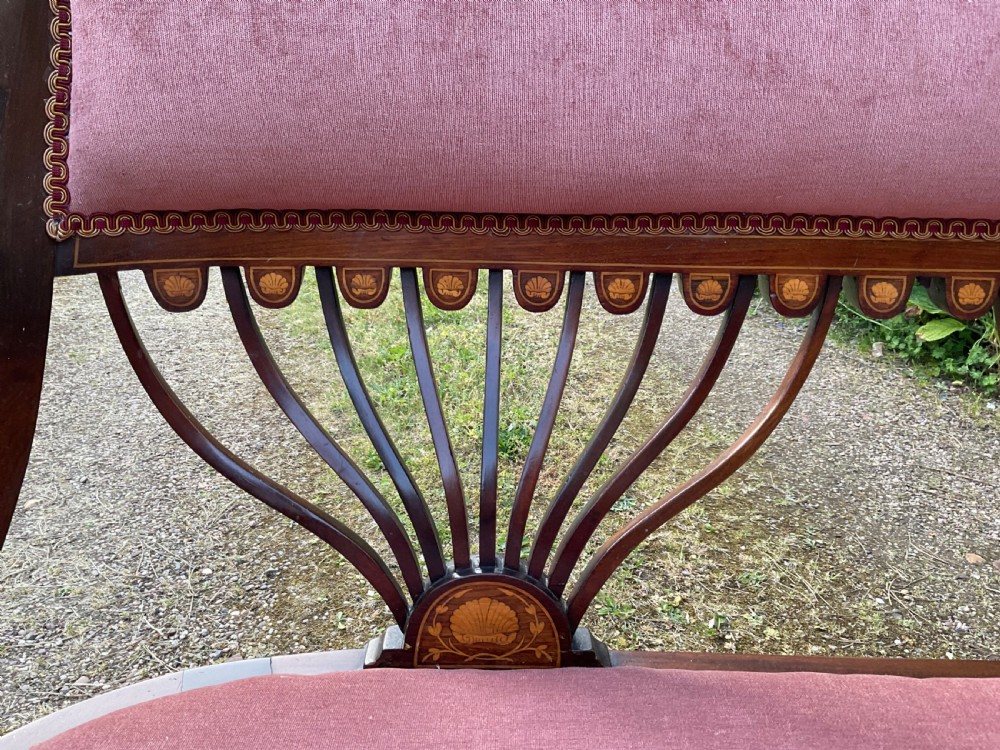 An Edwardian inlaid mahogany salon settee featuring a padded dusty pink velvet backrest and seat, flanked by sweeping arms and supported by splats with fan-shaped inlay. View IV