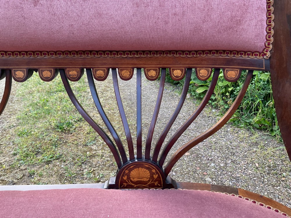 An Edwardian inlaid mahogany salon settee featuring a padded dusty pink velvet backrest and seat, flanked by sweeping arms and supported by splats with fan-shaped inlay. View VI