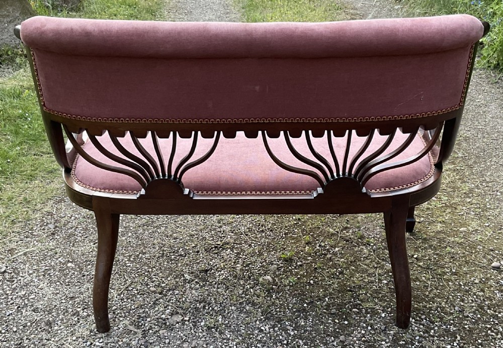 An Edwardian inlaid mahogany salon settee featuring a padded dusty pink velvet backrest and seat, flanked by sweeping arms and supported by splats with fan-shaped inlay. View VII