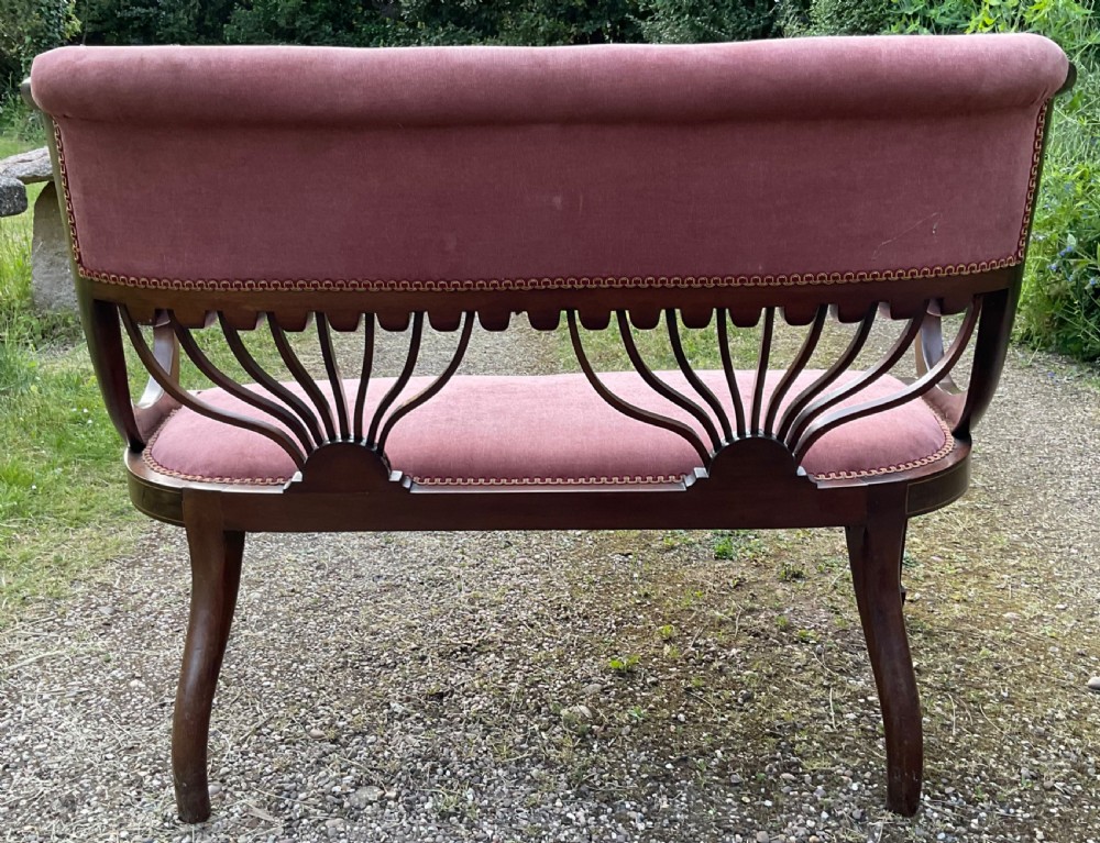 An Edwardian inlaid mahogany salon settee featuring a padded dusty pink velvet backrest and seat, flanked by sweeping arms and supported by splats with fan-shaped inlay. View VIII