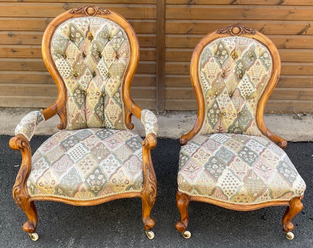 A pair of Victorian carved walnut salon chairs featuring deep buttoned patterned upholstery, spoon backs, scroll arms, and cabriole legs on castors.