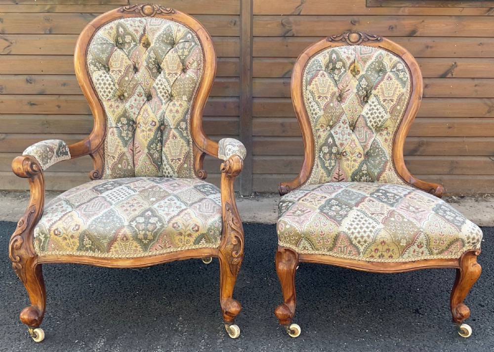 A pair of Victorian carved walnut salon chairs featuring deep buttoned patterned upholstery, spoon backs, scroll arms, and cabriole legs on castors. View II