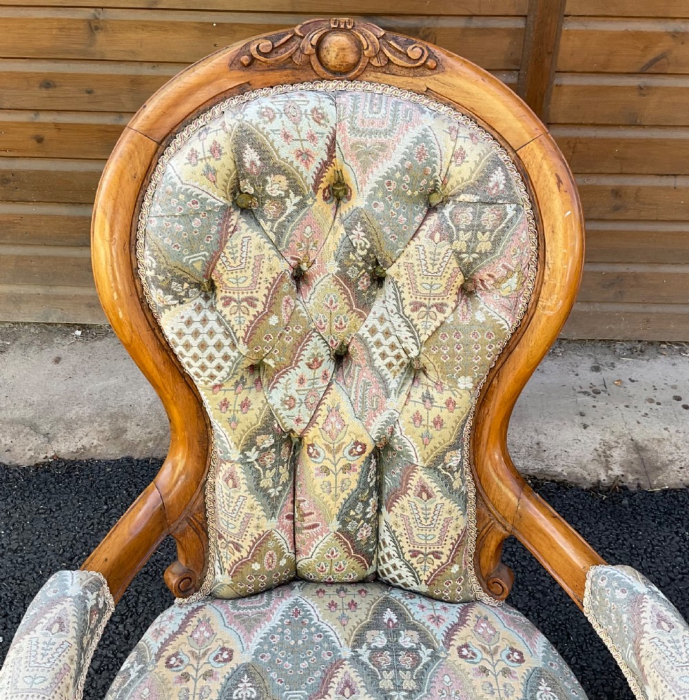 A pair of Victorian carved walnut salon chairs featuring deep buttoned patterned upholstery, spoon backs, scroll arms, and cabriole legs on castors. View III