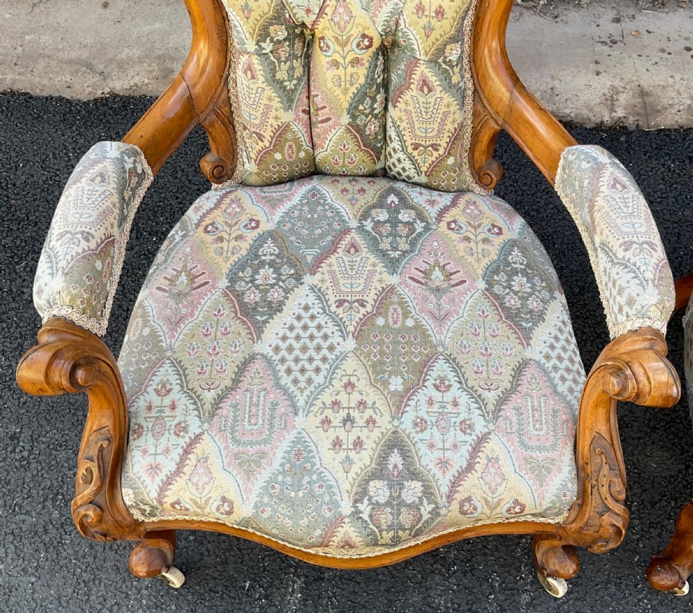 A pair of Victorian carved walnut salon chairs featuring deep buttoned patterned upholstery, spoon backs, scroll arms, and cabriole legs on castors. View IV