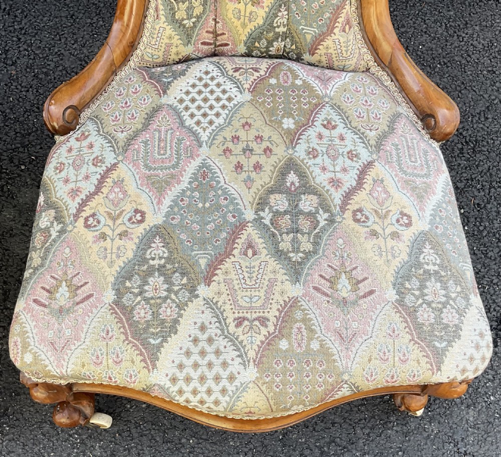 A pair of Victorian carved walnut salon chairs featuring deep buttoned patterned upholstery, spoon backs, scroll arms, and cabriole legs on castors. View VI