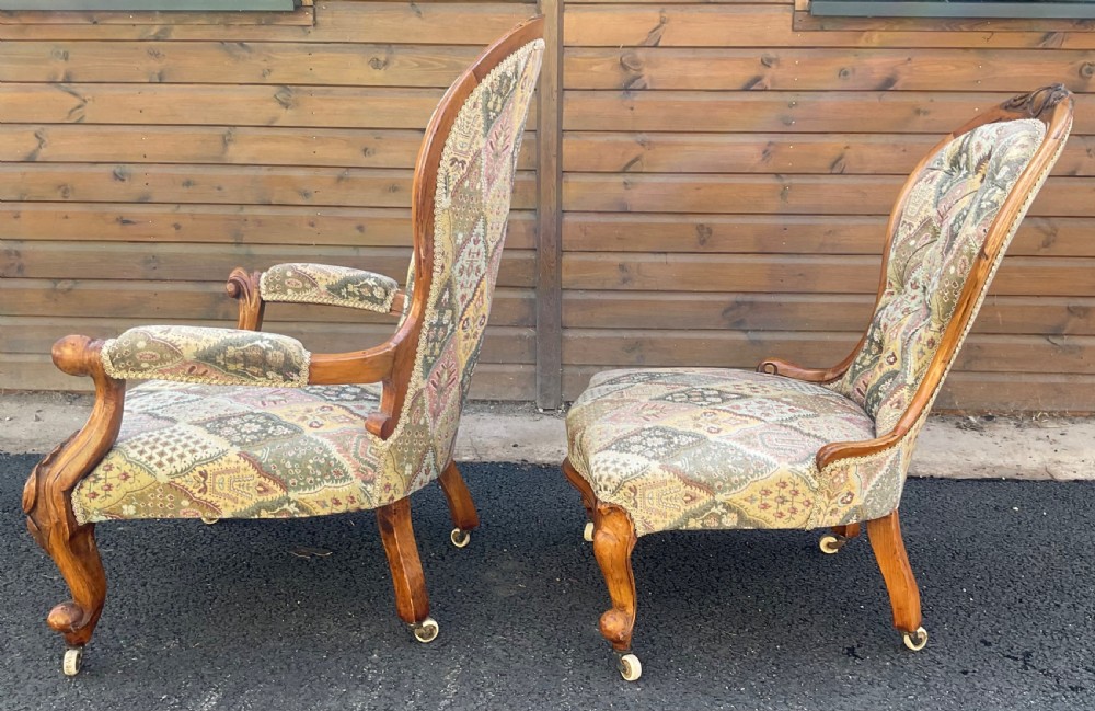 A pair of Victorian carved walnut salon chairs featuring deep buttoned patterned upholstery, spoon backs, scroll arms, and cabriole legs on castors. View VII