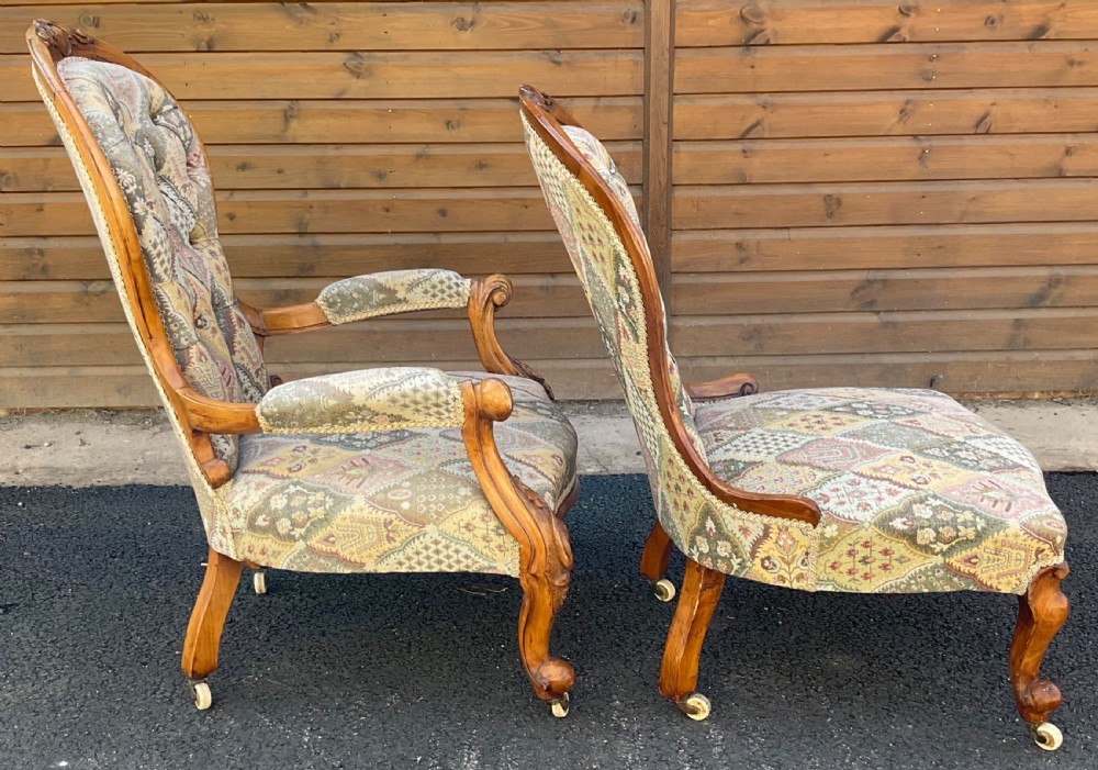 A pair of Victorian carved walnut salon chairs featuring deep buttoned patterned upholstery, spoon backs, scroll arms, and cabriole legs on castors. View X