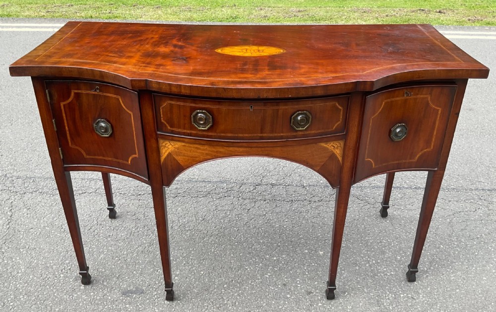 A Georgian mahogany bowfront sideboard featuring marquetry inlays, a central drawer, flanking cupboard doors, and tapered legs.