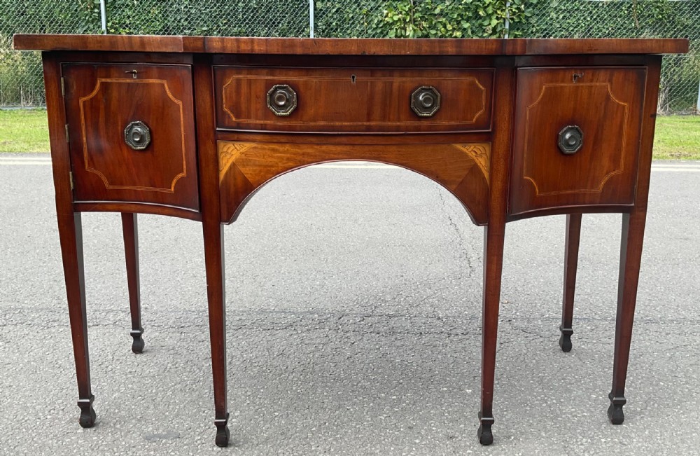 A Georgian mahogany bowfront sideboard featuring marquetry inlays, a central drawer, flanking cupboard doors, and tapered legs. View II