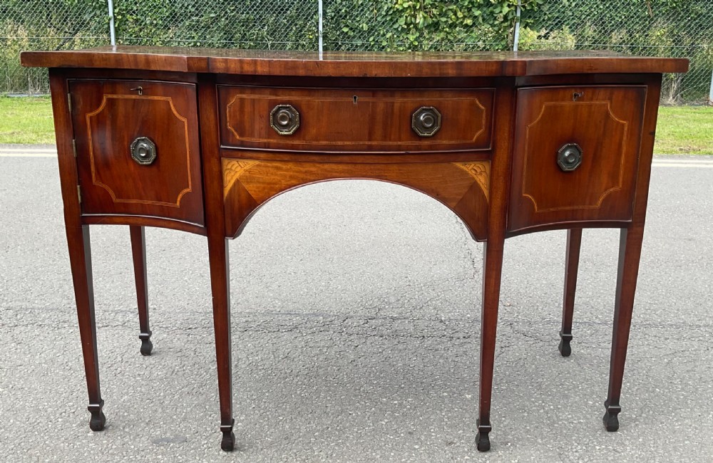 A Georgian mahogany bowfront sideboard featuring marquetry inlays, a central drawer, flanking cupboard doors, and tapered legs. View III