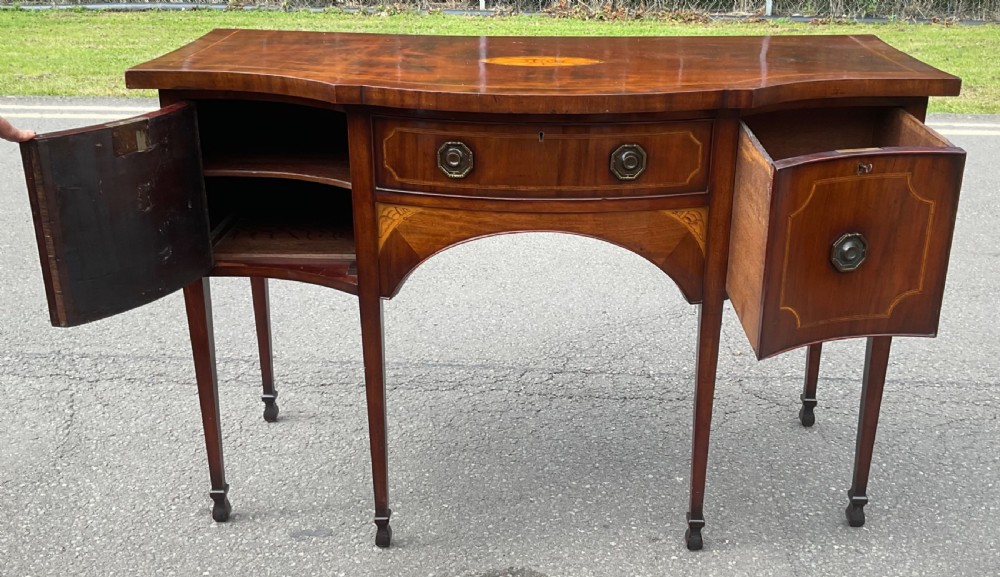 A Georgian mahogany bowfront sideboard featuring marquetry inlays, a central drawer, flanking cupboard doors, and tapered legs. View V