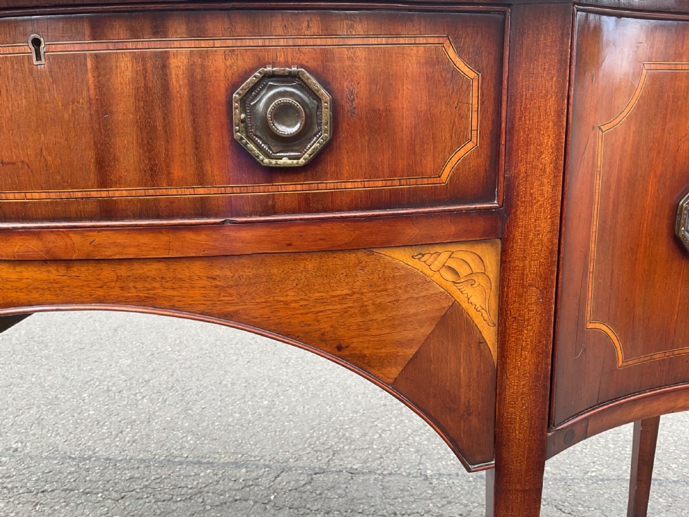 A Georgian mahogany bowfront sideboard featuring marquetry inlays, a central drawer, flanking cupboard doors, and tapered legs. View VIII