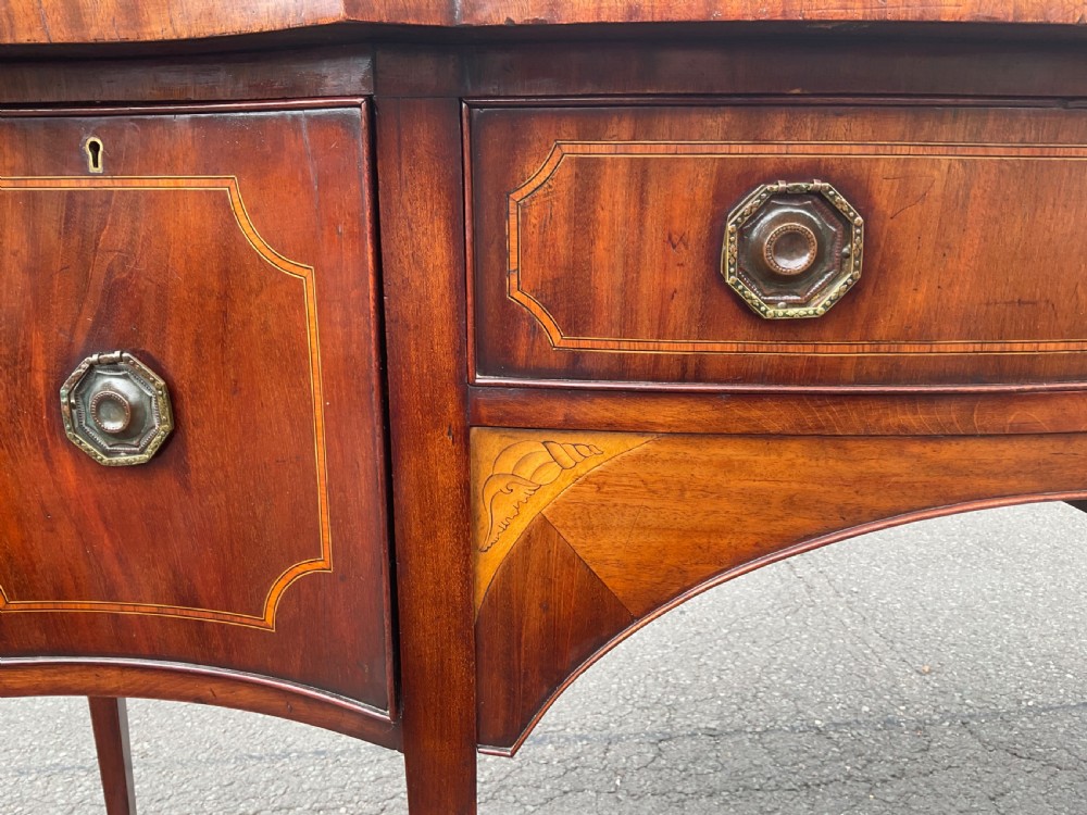 A Georgian mahogany bowfront sideboard featuring marquetry inlays, a central drawer, flanking cupboard doors, and tapered legs. View IX