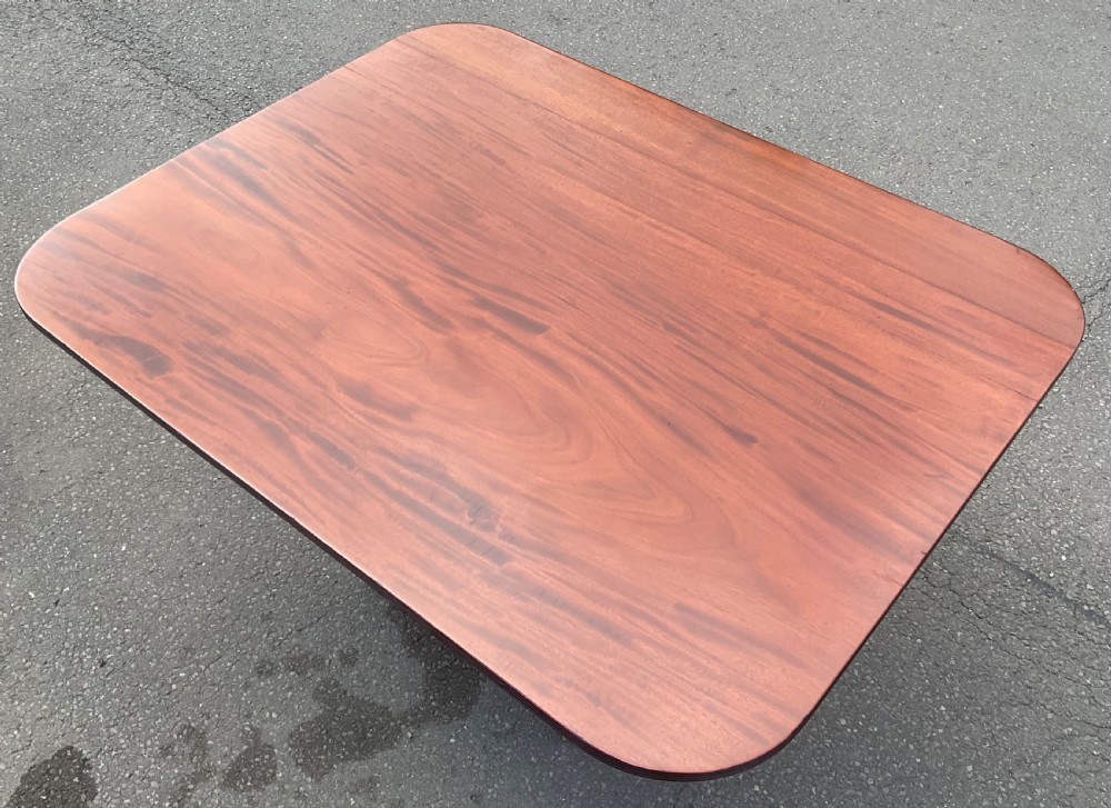 A Georgian mahogany pedestal table featuring a rectangular top with rounded edges, a turned central column, and four splayed reeded legs on brass castors. View IX