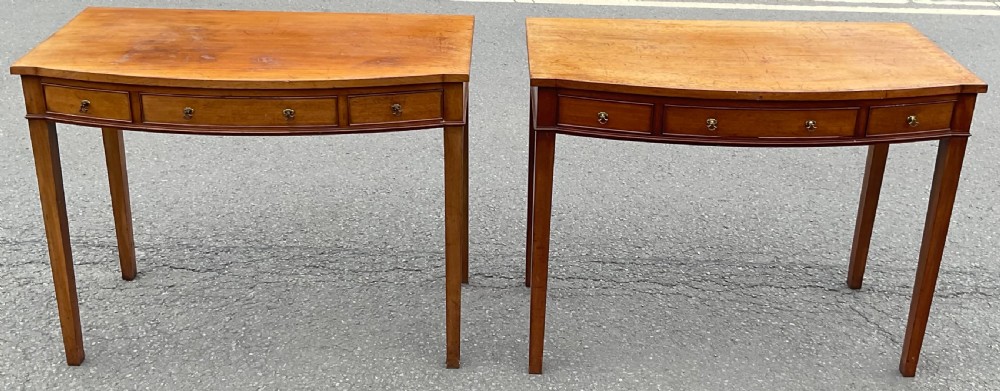 A pair of Georgian-style mahogany side tables featuring gentle bowfronts, drawer fronts with brass ring handles, and square tapered legs.