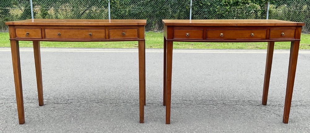 A pair of Georgian-style mahogany side tables featuring gentle bowfronts, drawer fronts with brass ring handles, and square tapered legs. View III