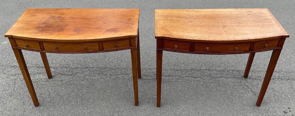 A pair of Georgian-style mahogany side tables featuring gentle bowfronts, drawer fronts with brass ring handles, and square tapered legs. View IV