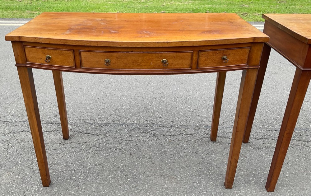 A pair of Georgian-style mahogany side tables featuring gentle bowfronts, drawer fronts with brass ring handles, and square tapered legs. View V