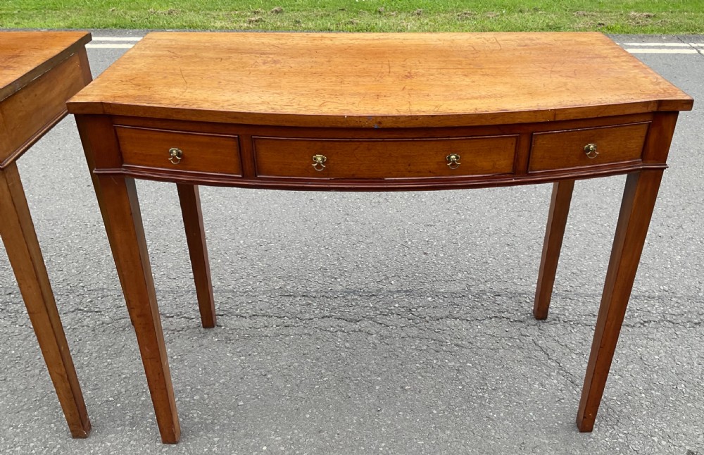 A pair of Georgian-style mahogany side tables featuring gentle bowfronts, drawer fronts with brass ring handles, and square tapered legs. View VI