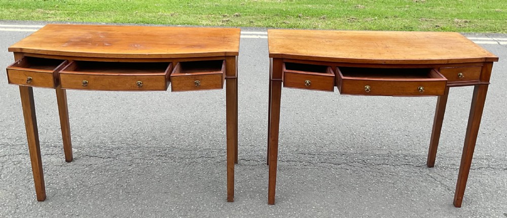 A pair of Georgian-style mahogany side tables featuring gentle bowfronts, drawer fronts with brass ring handles, and square tapered legs. View XI