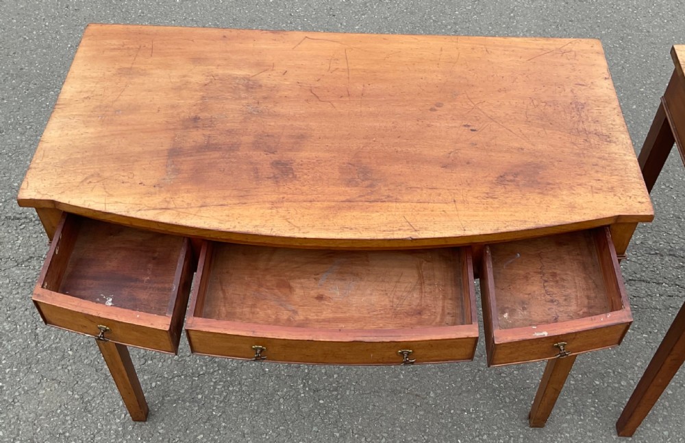 A pair of Georgian-style mahogany side tables featuring gentle bowfronts, drawer fronts with brass ring handles, and square tapered legs. View XII