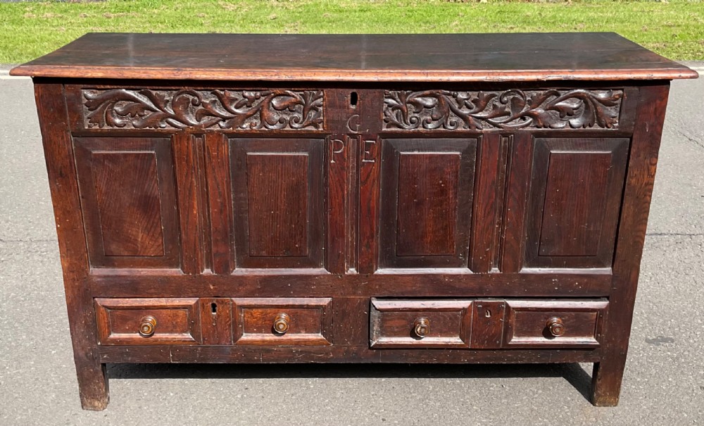 A dark oak Georgian mule chest featuring a hand-carved floral frieze, carved initials, four fielded front panels, and two base drawers with turned knobs.