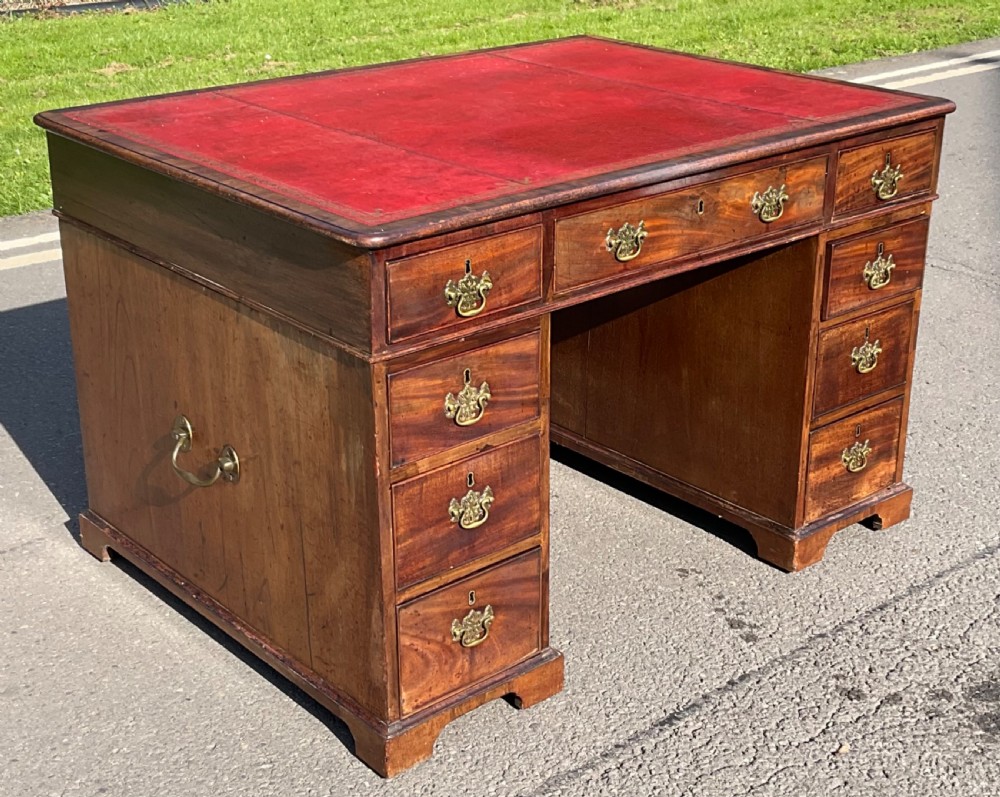 A Georgian mahogany partners desk featuring a red leather inset top, brass handles on multiple drawers, side carrying handles, and bracket feet.