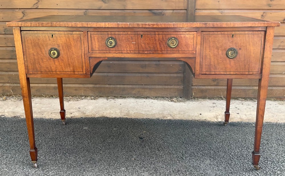 An Edwardian mahogany writing table featuring a dark leather inset top, three brass-handled drawers, tapered square legs, and brass castors.