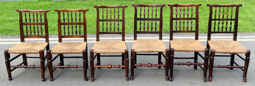 A set of six Georgian dark elm country dining chairs featuring turned spindle backrests and woven rush seats.
