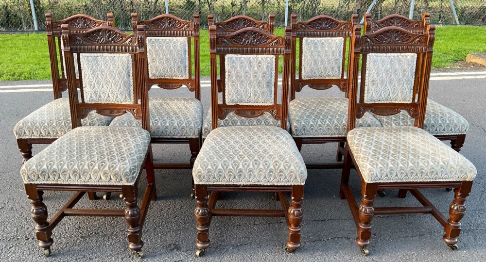 A set of eight Edwardian carved oak dining chairs with patterned fabric upholstery, turned legs, and brass castors.