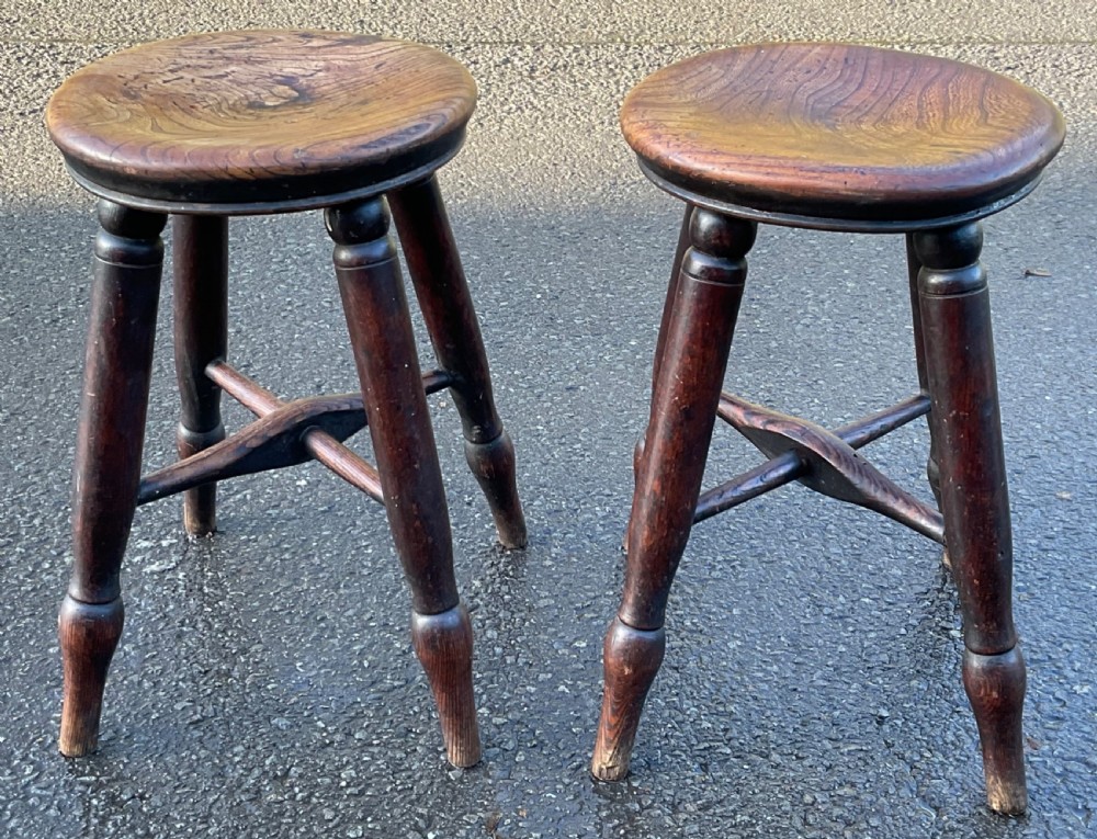 A pair of Victorian country wooden stools featuring circular elm seats, turned legs, and cross stretchers in a dark brown finish.