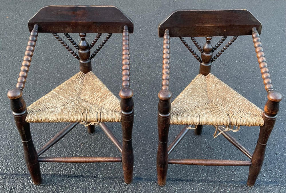 A pair of antique dark wood corner armchairs featuring triangular woven rush seats and detailed bobbin-turned arms and backrests.