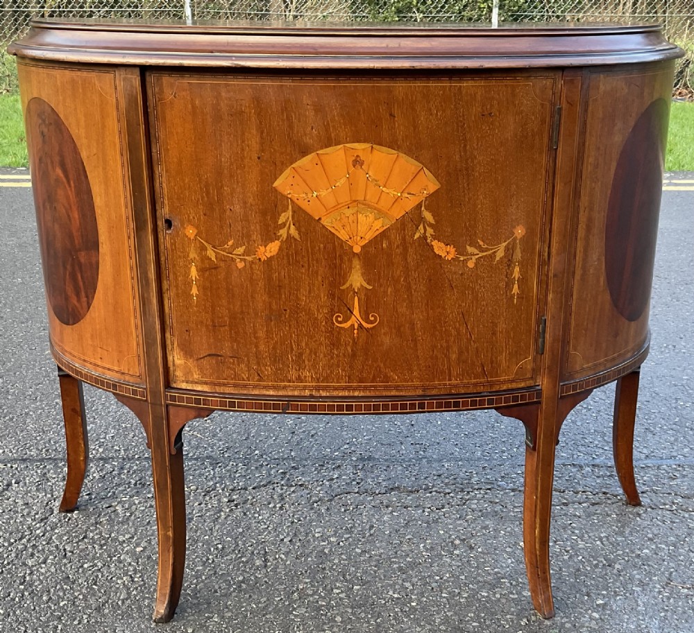 An Edwardian bowfront mahogany side cabinet featuring intricate fan marquetry and floral swags on slender curved legs.