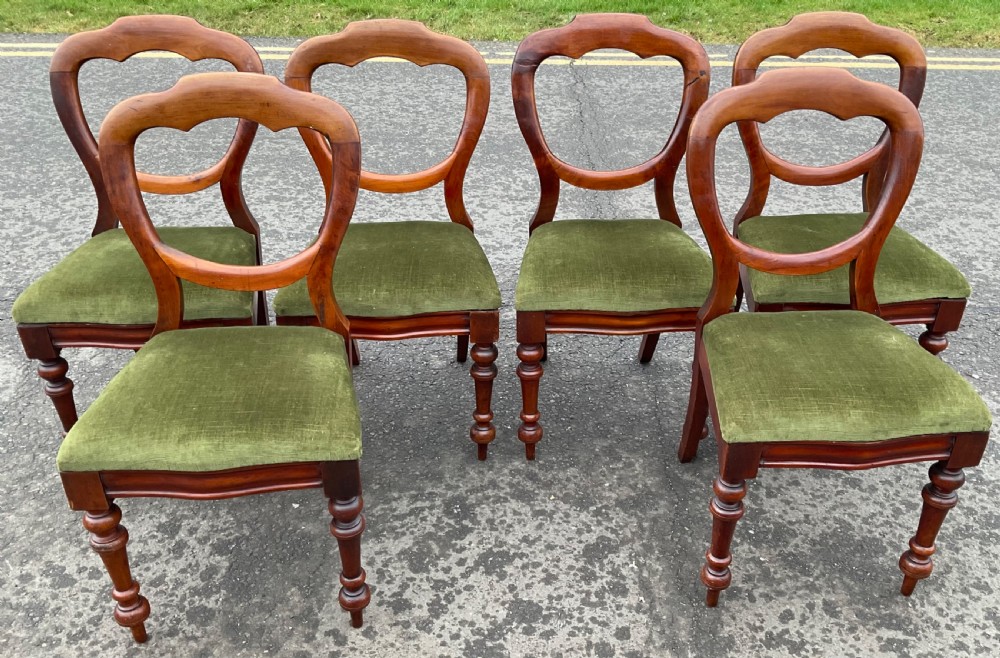 A set of six Victorian mahogany balloon back dining chairs featuring turned front legs and green velvet upholstered seats.