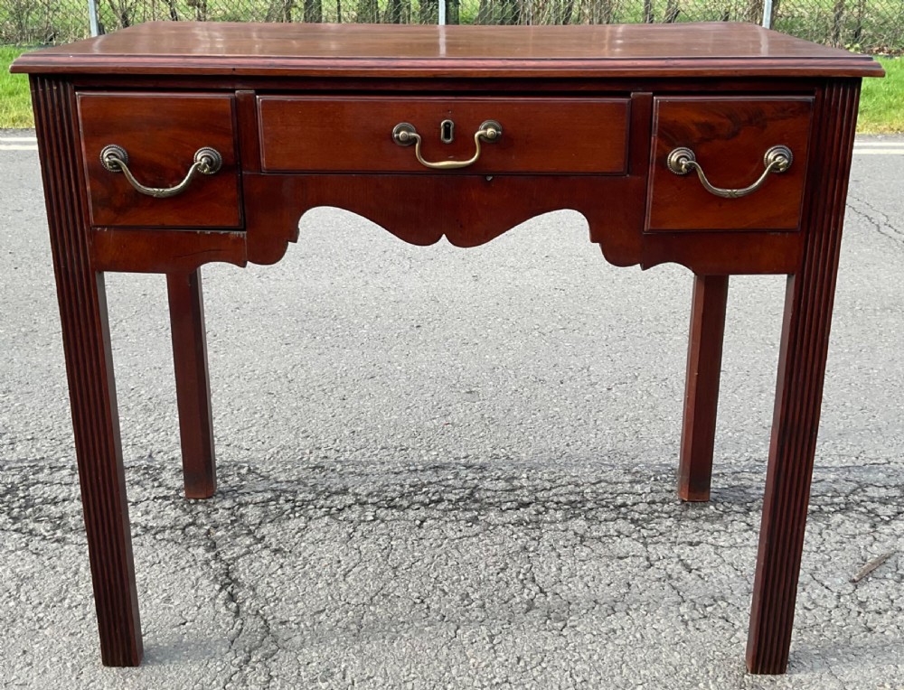A Georgian mahogany side table featuring three front drawers with brass swan-neck handles, a shaped apron, and fluted square legs.