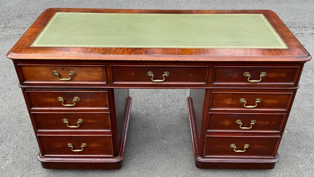 A Victorian mahogany pedestal writing desk featuring nine drawers with brass swan-neck handles and a green gold-tooled leather writing surface.