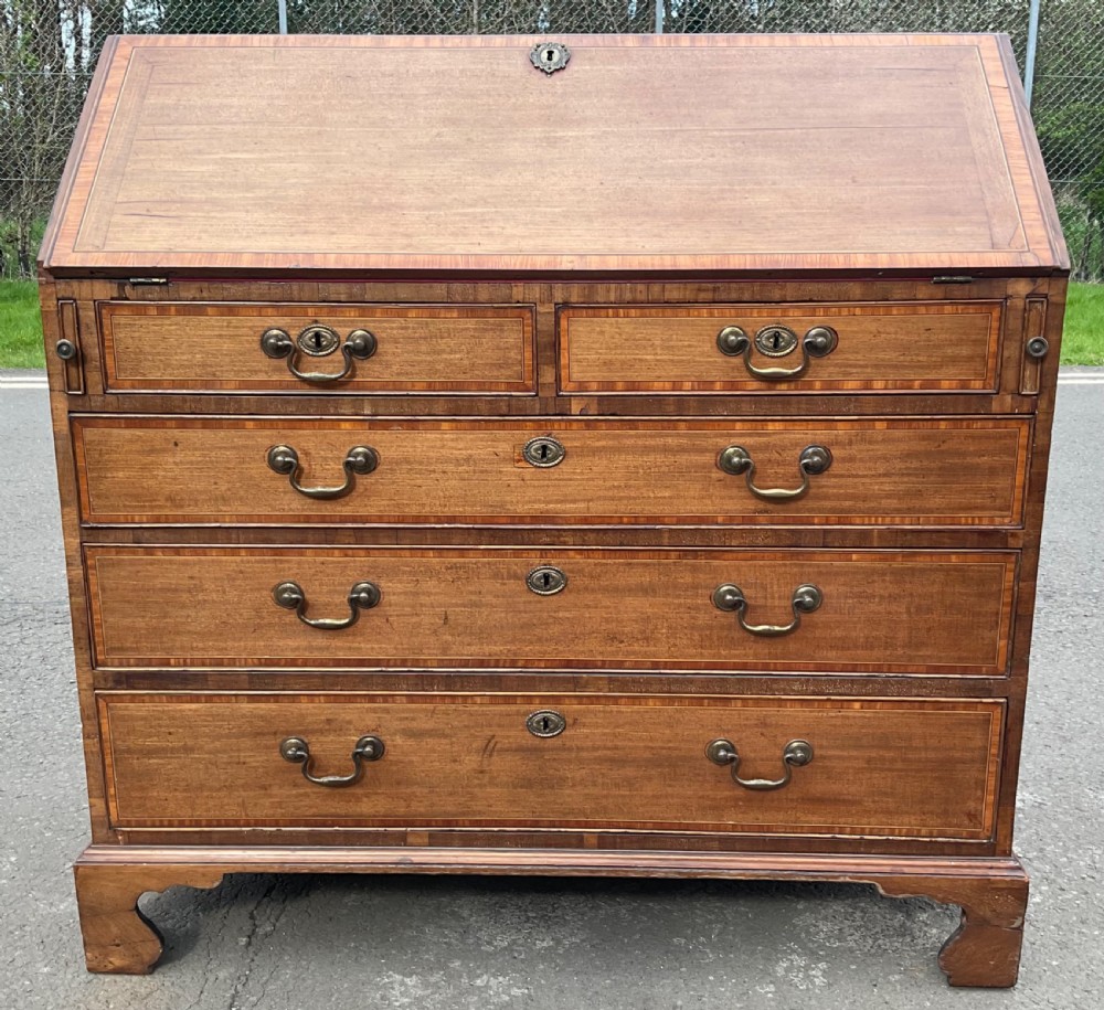An antique Georgian mahogany writing bureau featuring a slanted fall-front lid, satinwood crossbanding inlay, brass swan-neck handles, and bracket feet.