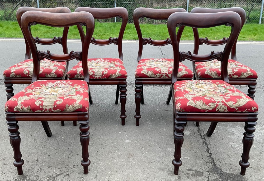 A set of six Victorian mahogany dining chairs featuring rounded balloon backs, carved cross rails, red floral fabric upholstery, and turned front legs.