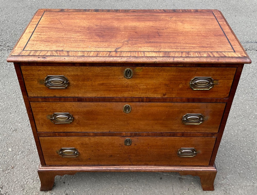 A small Georgian mahogany chest of three graduated drawers with crossbanded inlay, brass handles, and bracket feet.